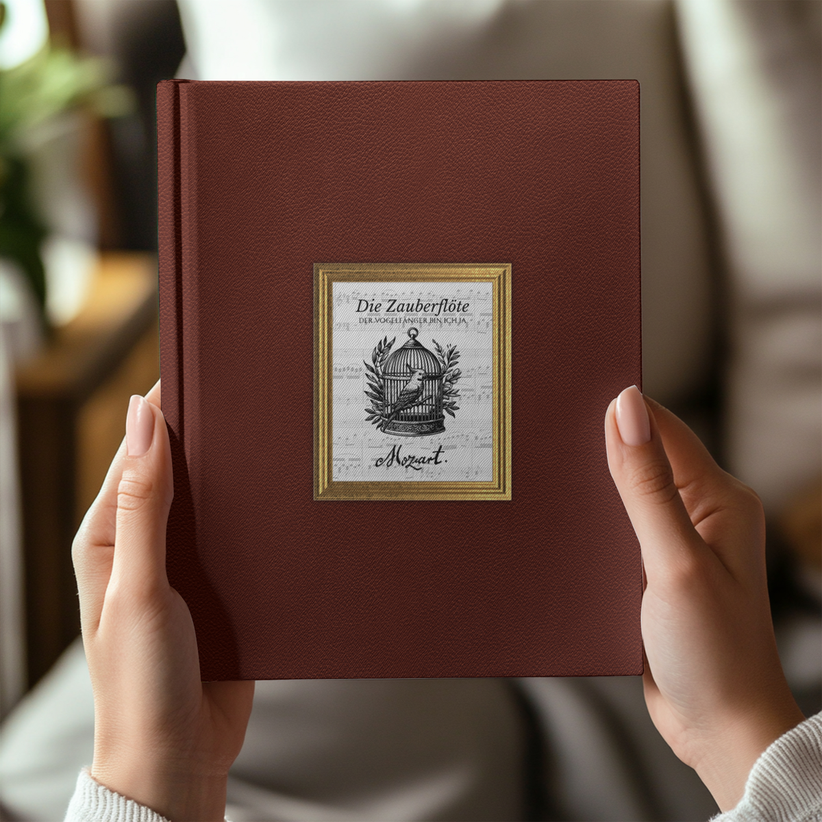Hands hold a Magic Flute journal in burgundy with a birdcage illustration